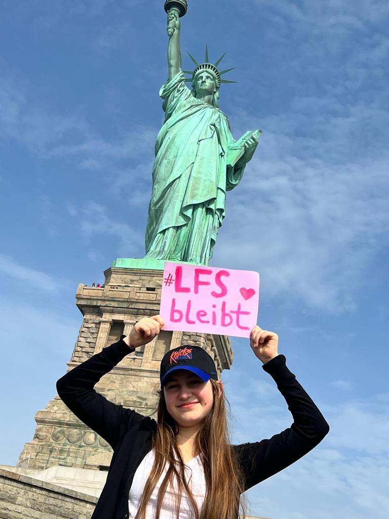 Mädchen vor der Freiheitsstatue in New York mit einem LFS bleibt Plakat