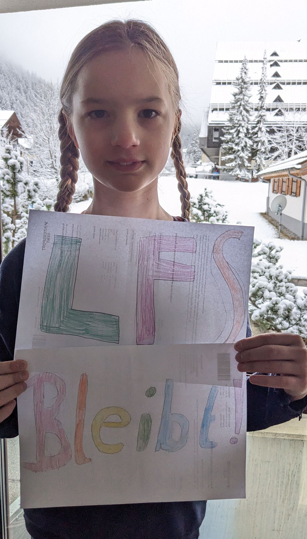 Ein Mädchen mit LFS Plakat vor einer Schneelandschaft.