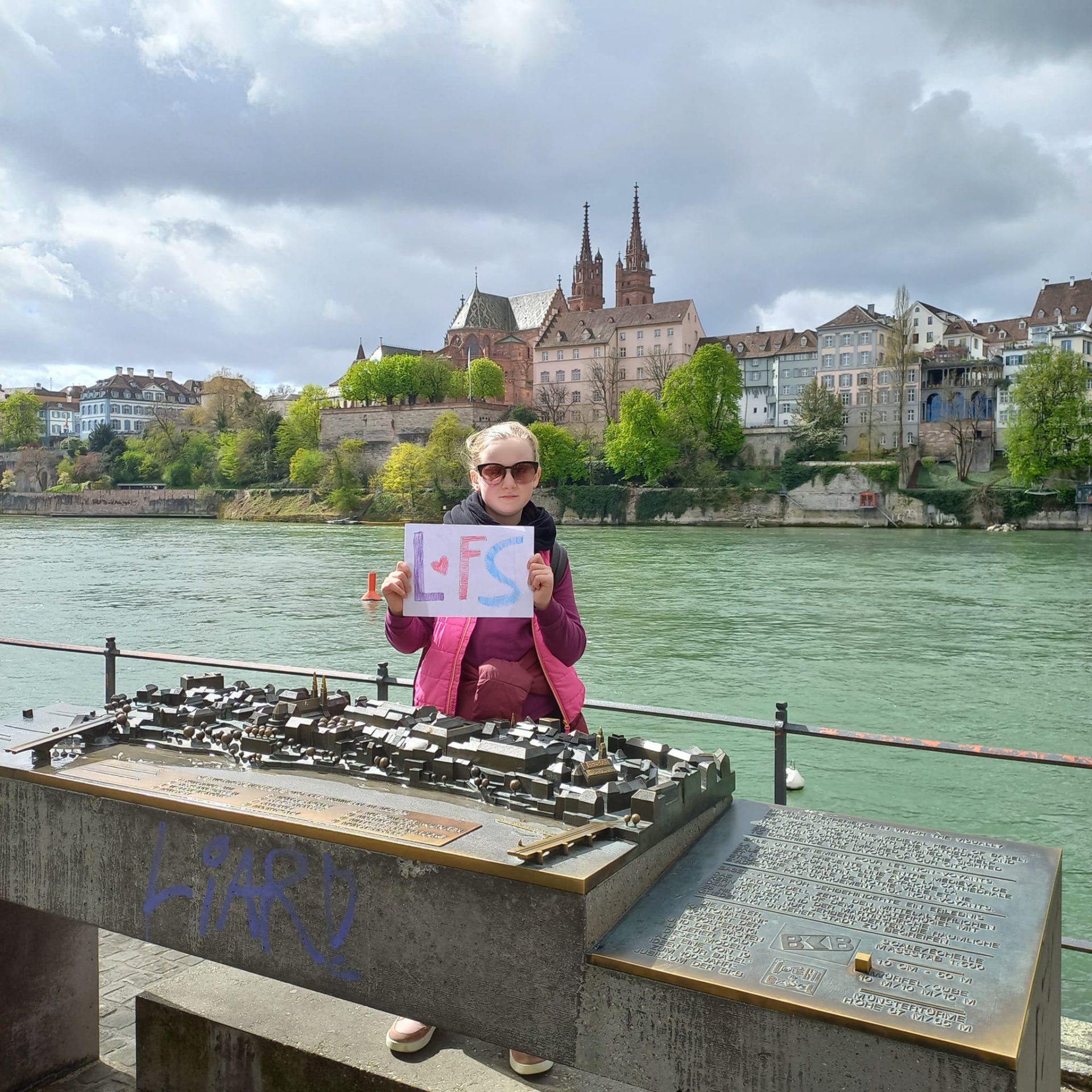 Ein Mädchen steht mit einem LFS Plakat in Basel am Fluß.