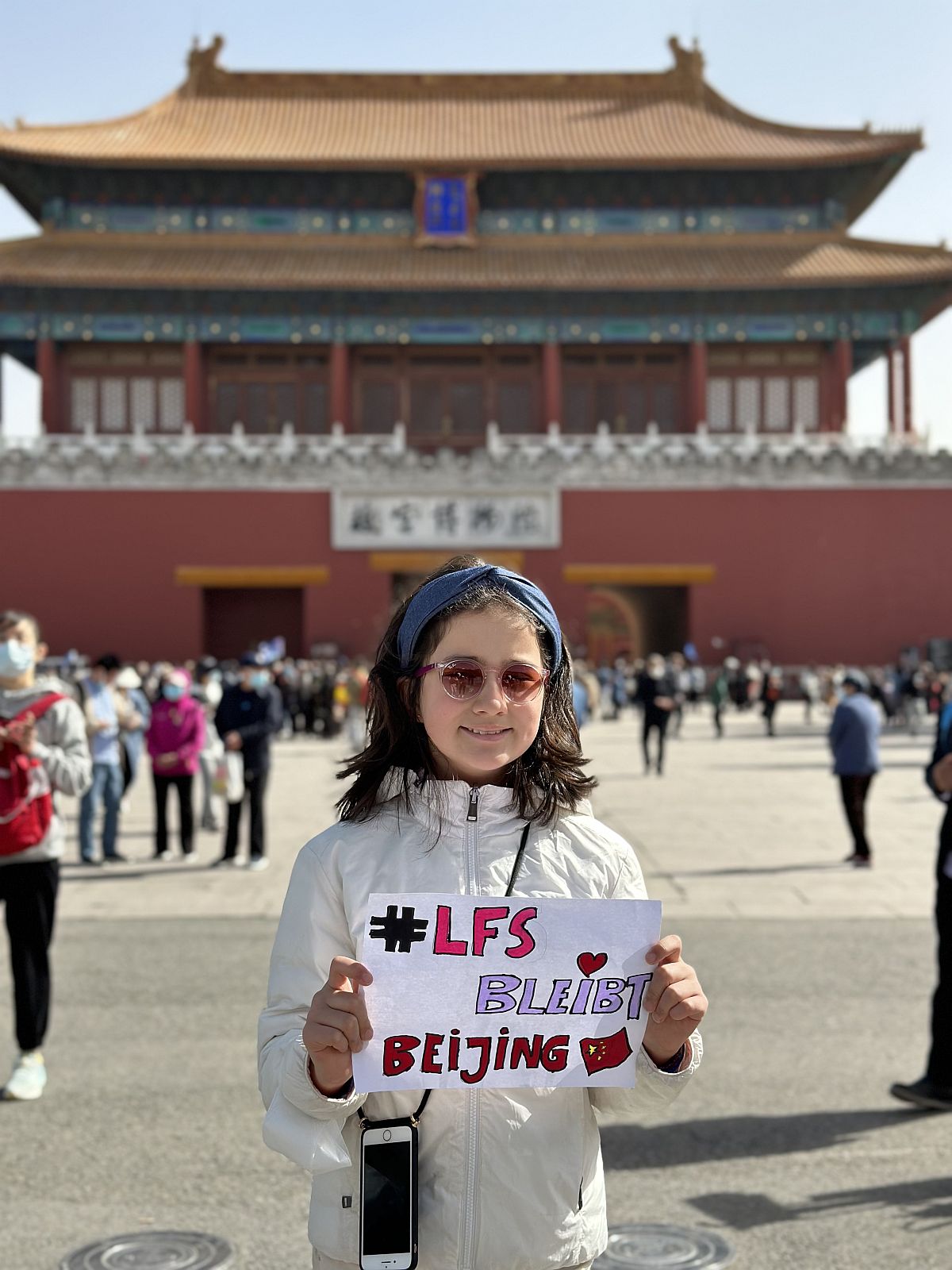 Ein Mädchen steht mit einem LFS bleibt Plakat vor der Verbotenen Stadt in Beijing